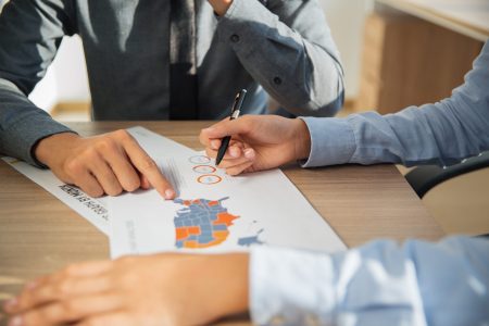 Unrecognizable business people sitting at table indoors and studying statistic report on USA. Businessman pointing at document and businesswoman holding pen